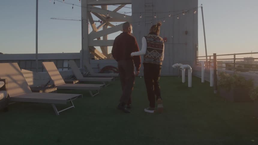 People walk side by side on a rooftop with artificial grass and lights at sunset