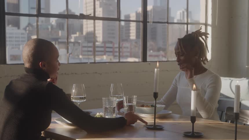 Couple shares candlelit dinner in apartment with city view exchanging smiles in a cozy naturally lit setting