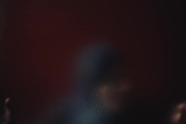 Person appears blurred with hand pressed against translucent surface in a dark setting