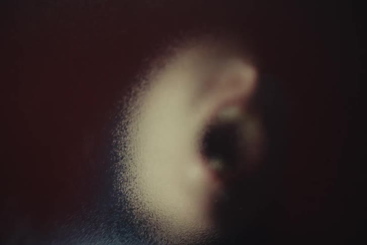 Mouth pressed against translucent surface appears blurred in intense expression