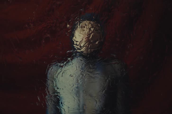 Blurred silhouette behind wet glass reveals subtle contours amid warm tones