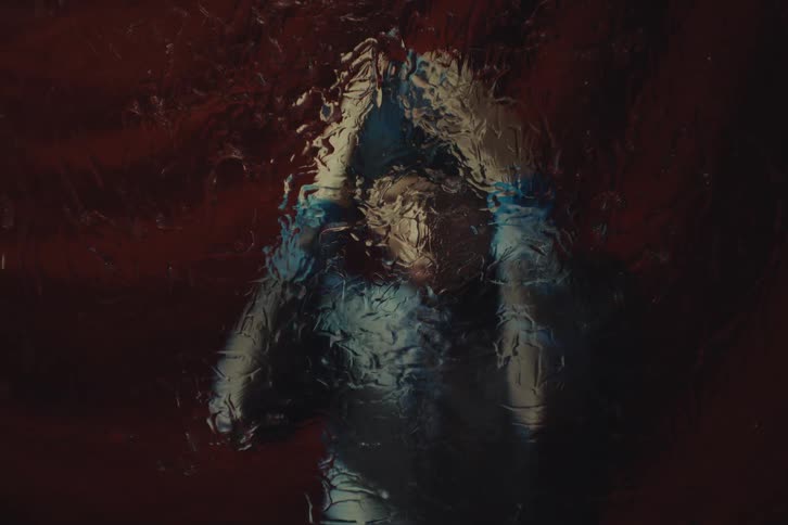 Distorted figure behind wet glass emerges amid warm tones and soft shadows
