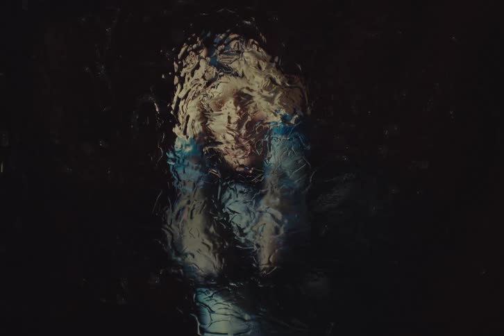 Person with hands on their head appears distorted through a watercovered glass
