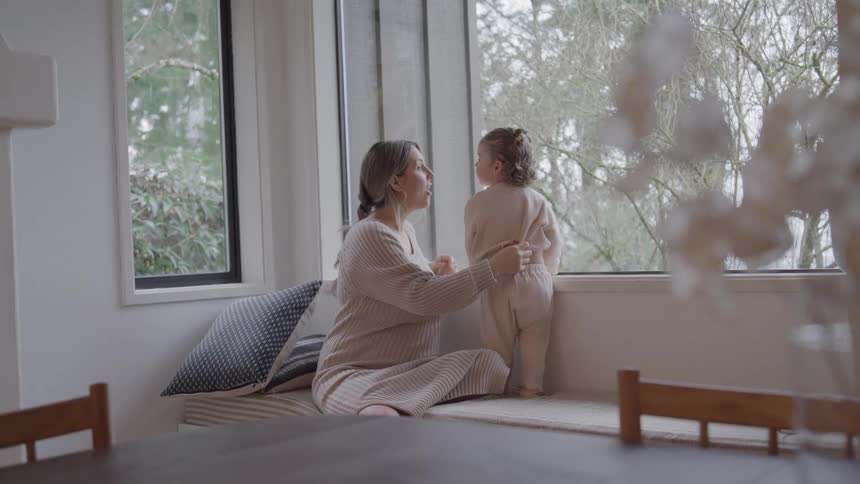 Woman and child look at the landscape through a large window in a cozy setting