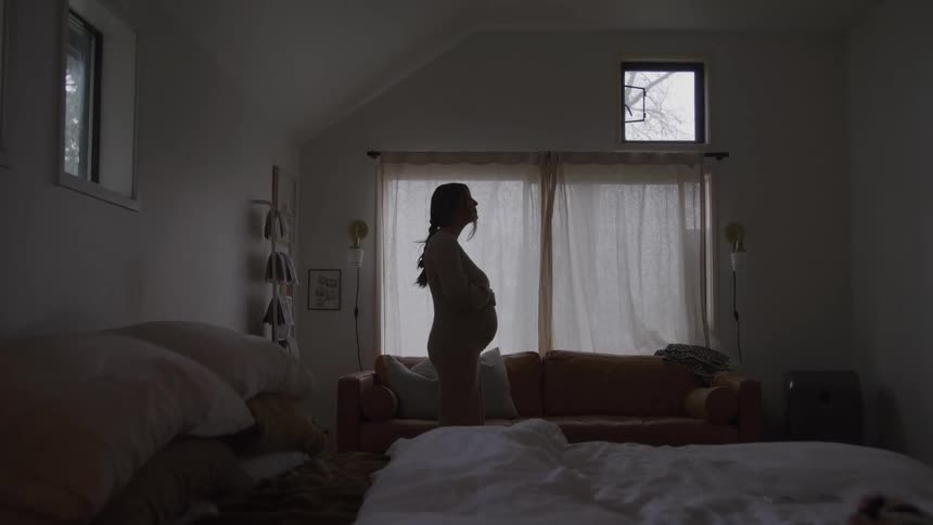 Woman standing by the window with hands on belly in residential setting