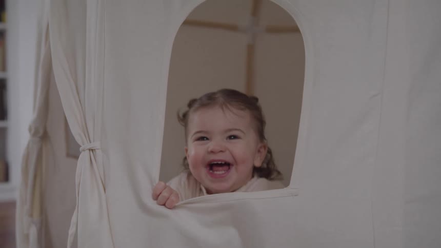 Child smiles excitedly while peeking through the window of a play tent