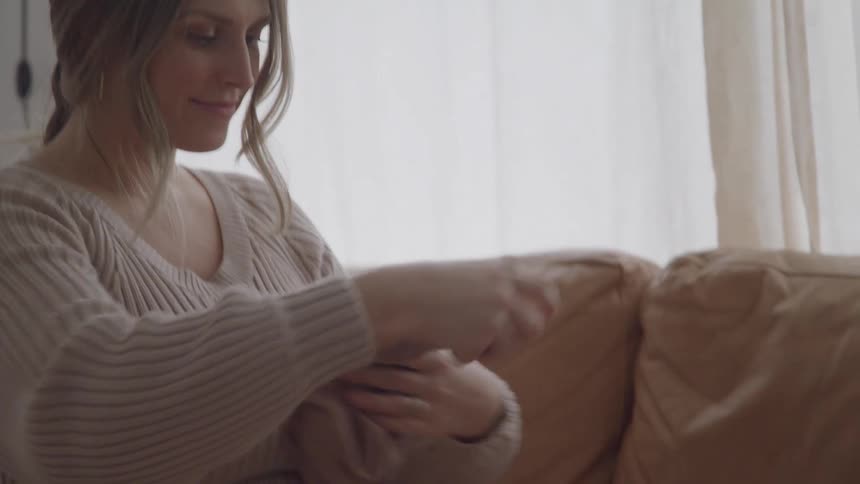 Woman holds a piece of clothing with a calm expression in a bright setting