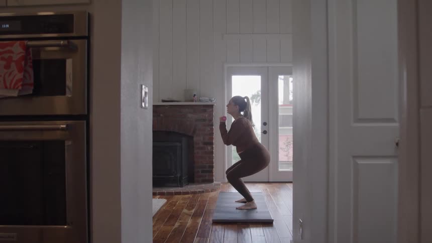 Pregnant person performing squat exercise in residential setting with natural lighting