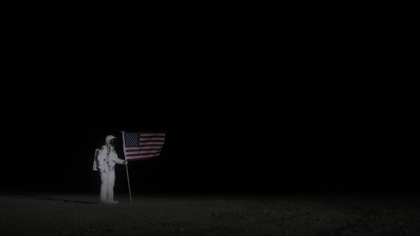 Astronaut holds an american flag in a dark and desolate landscape
