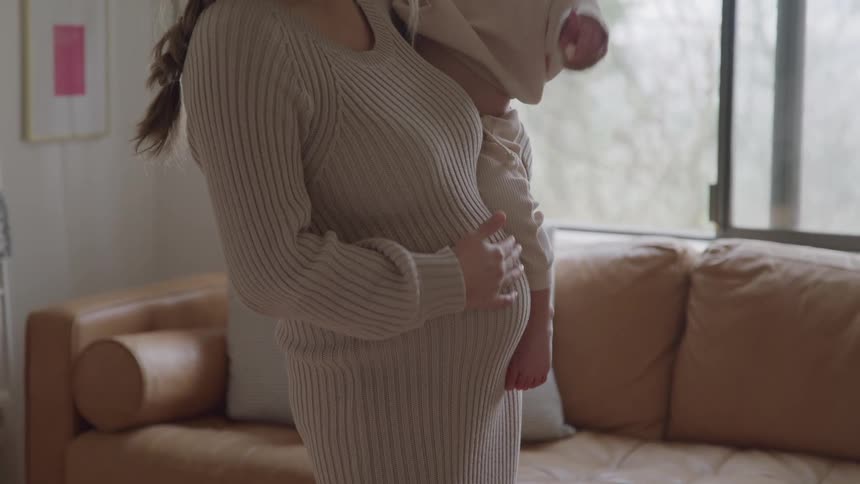 Pregnant mother holds her young daughter in her arms in a cozy setting
