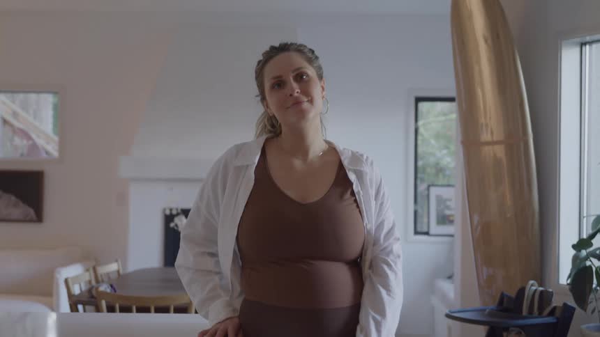The pregnant woman turns her head from the window and smiles