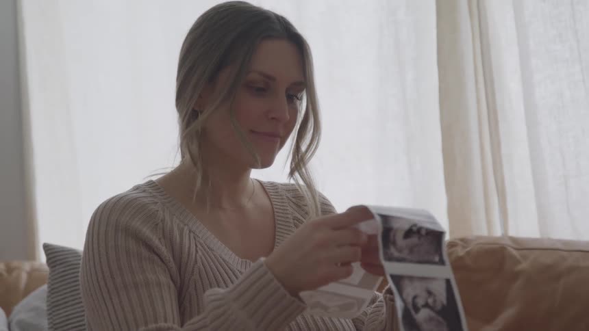 Woman looks at ultrasound images with a serene and emotional expression