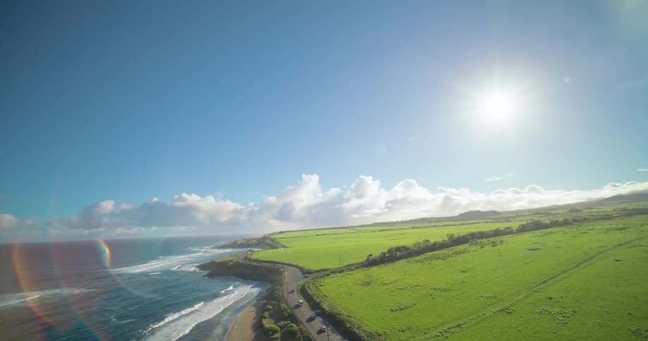 Winding coastal road follows the meeting of the blue sea with vast green fields