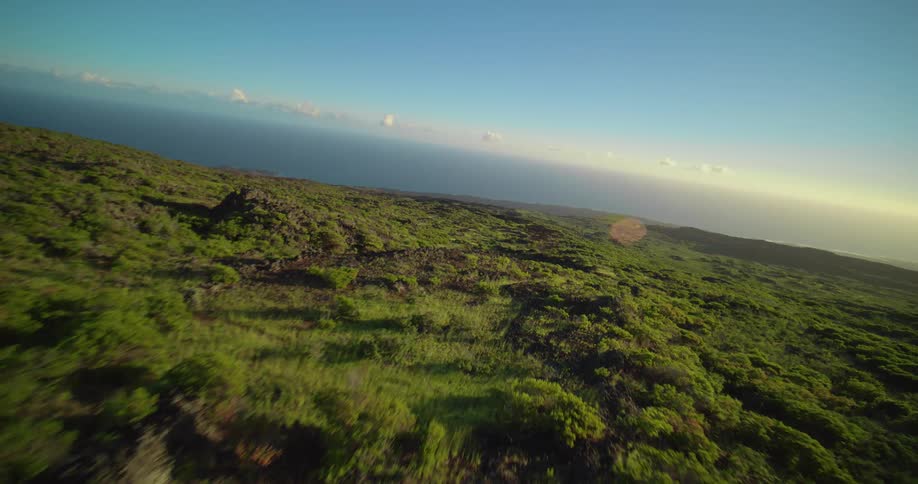 Lush green landscape stretches beneath a blue sky lit by the sun