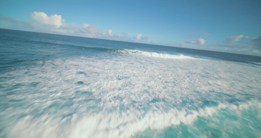 Blue waves move toward a rocky shore under a clear and sunny sky