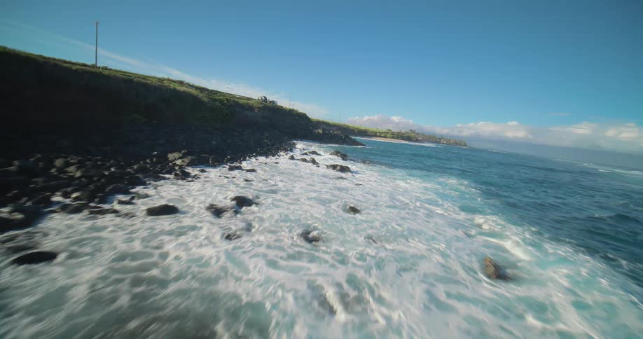 Foamy blue waves approach the shore under a clear and sunny sky