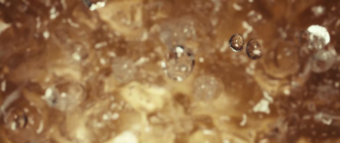 A macro close view shows liquid bubbles rising rapidly in a carbonated goldenbrown liquid with a blurred bubbling background