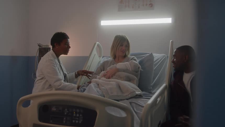 Woman holds a newborn in a hospital bed beside a man and a healthcare professional