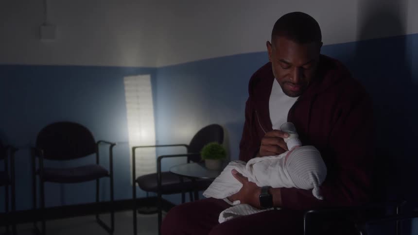 Man feeds a newborn in his arms in a quiet room