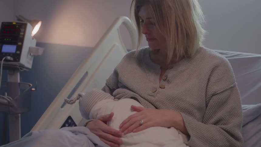 Mother gently holds her newborn in a hospital bed