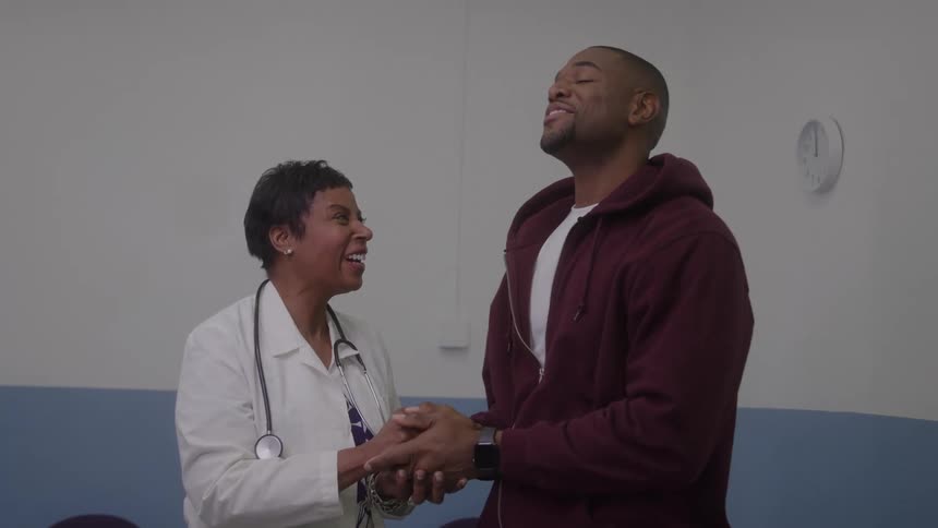 Healthcare professional in white coat holding hands of person in maroon hoodie in clinical setting