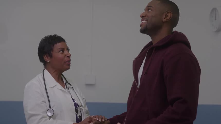 A female black doctor conversing with a young black man while standing together in a room