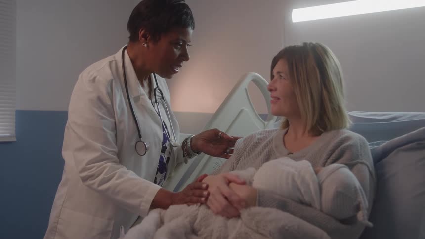 Doctor talks with a mother holding her newborn in bed