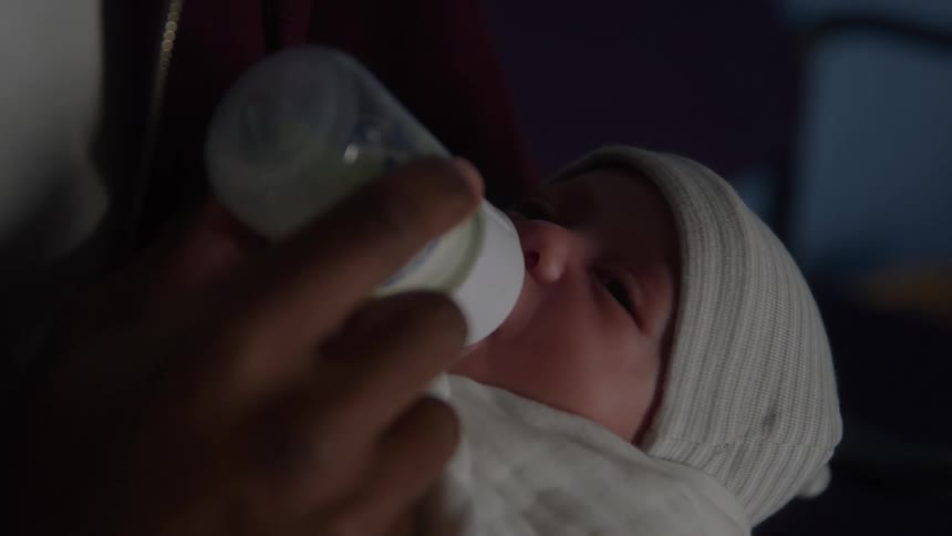 A baby is fed with a bottle by an adult