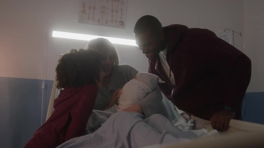 The family smile while looking at the newborn in the hospital