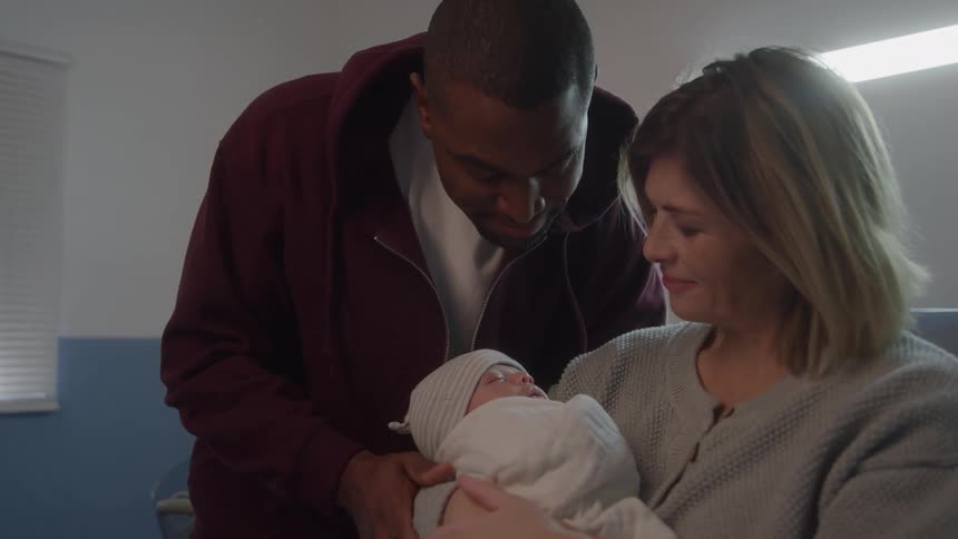 A couple admires their newborn baby wrapped in a blanket at the hospital