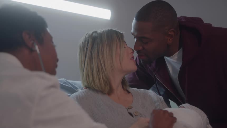 Husband and wife kissing as she sits in hospital bed after giving birth