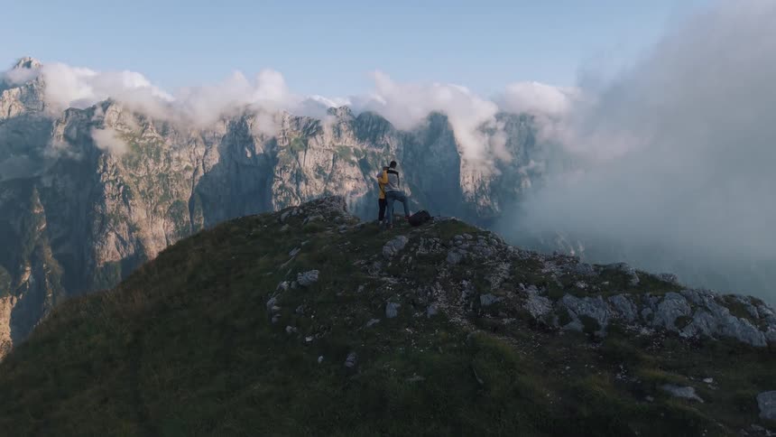 Couple hugging with backpack enjoys the view of the mountains among clouds