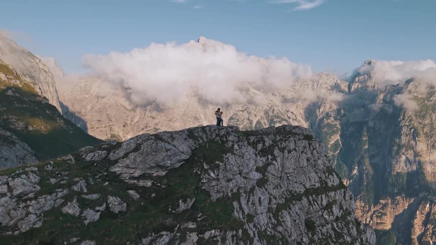 A person stands at the top of a mountain during a hike surrounded by rugged terrain at midday