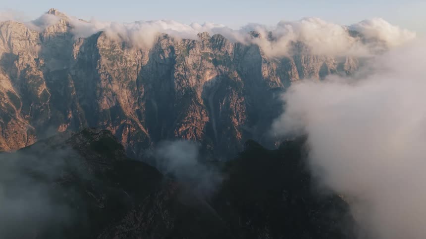 Rocky peaks shrouded in clouds emerge bathed in the soft light of dawn