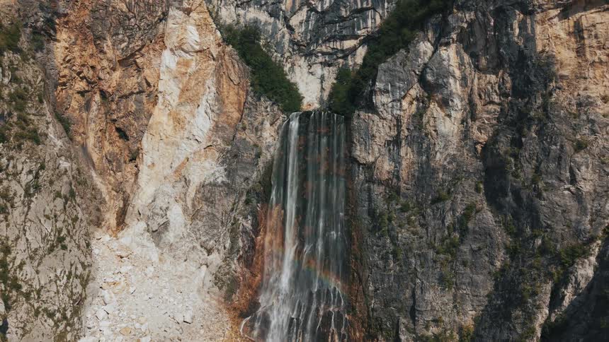 Waterfall flows down the rocks forming a rainbow in the sunlight
