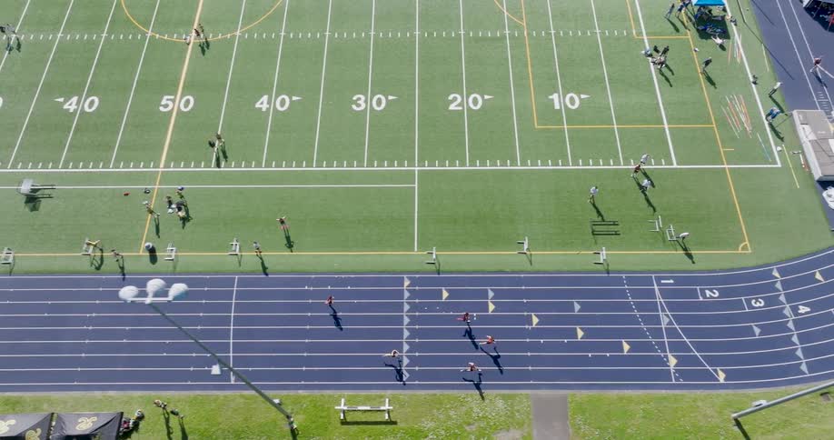 Traverse above athletes running in lanes along a track during a competitive meet