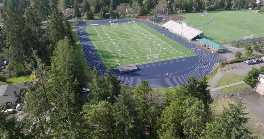 Tilt up reveal of a mostly empty high school athleic complex with several people walking on the track