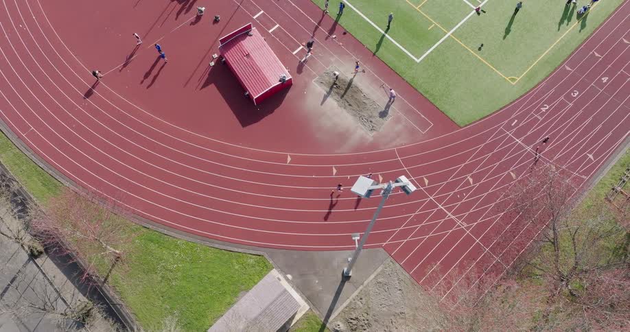 Three athletes round a bend competing on an outdoor running track during an early spring meet