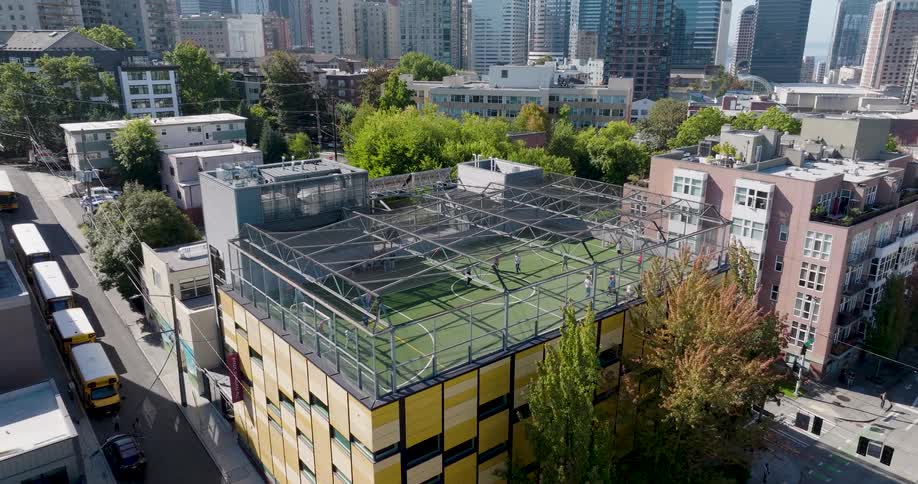 Kids play and excercise on a rooftop athletic field located in an urban area near downtown