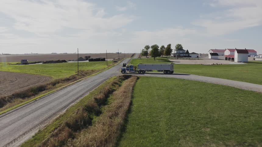 Metal silo with visible label beside rural road and parked vehicles in the background
