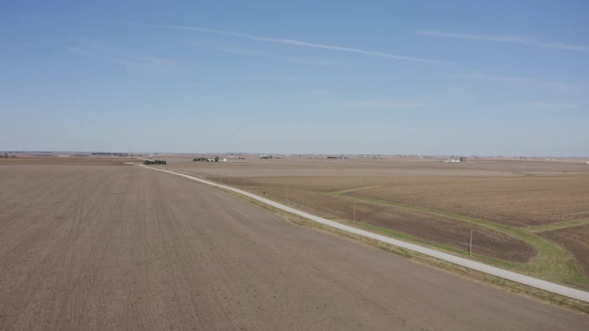 Paved road cuts through flat fields with power poles lining the route