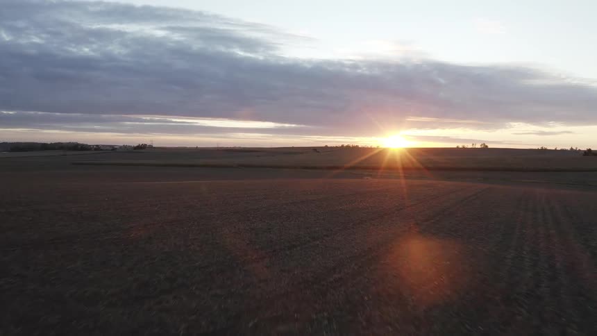 Plowed field under partly cloudy sky lit by the golden light of sunset