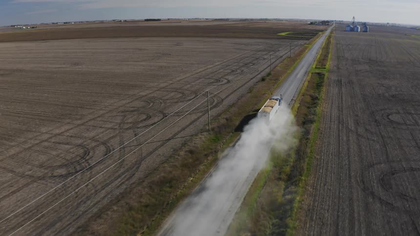 The truck transporting crops leaves a dust cloud as it drives