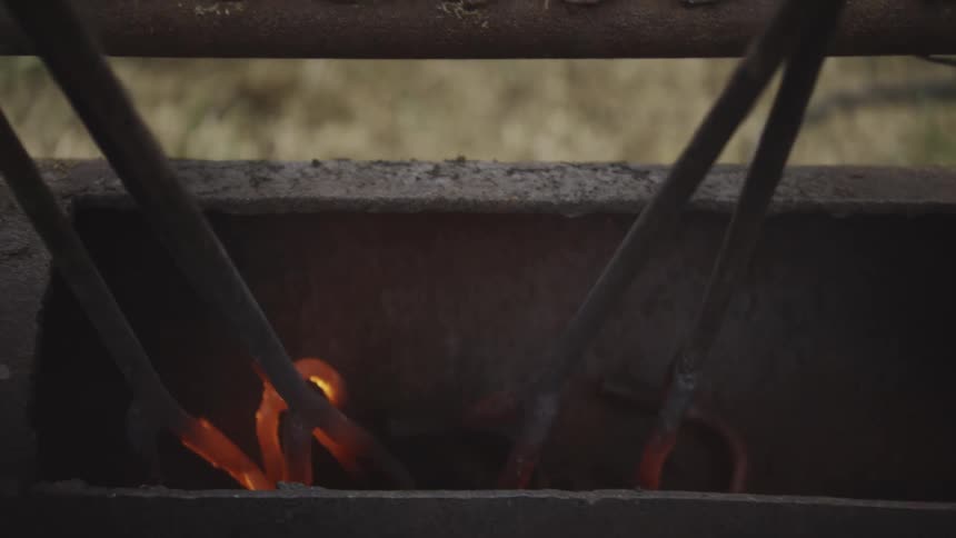 Metal tools being heated in forge with glowing embers