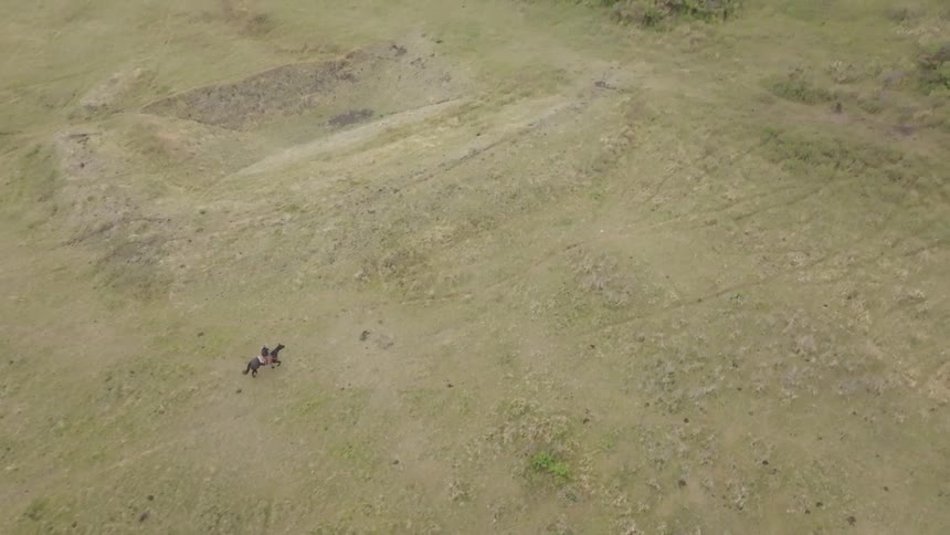 Lone rider crosses rolling terrain with sparse vegetation under cloudy sky