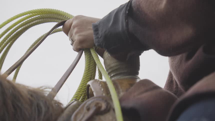 Closeup of a riders hand in a dark sleeve coils neongreen rope while sitting on a horse