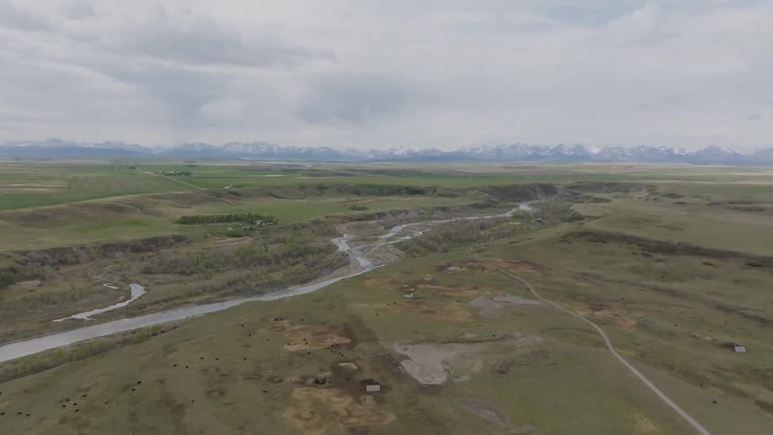 River winds through rural landscape with fields dense vegetation and snowcapped mountains in the distance