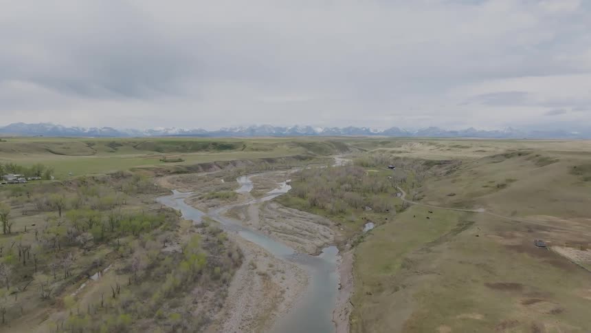 A river winds through an open expanse of grassland in the wild at midday