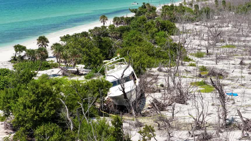 Boat stranded among trees and dunes on white sand beach with turquoise water