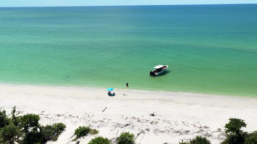 Aerial view of a boat by a white sand beach with people near the shore